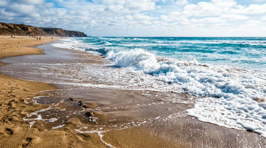 Ocean waves rolling onto a sandy beach with cliffs and people in the distance